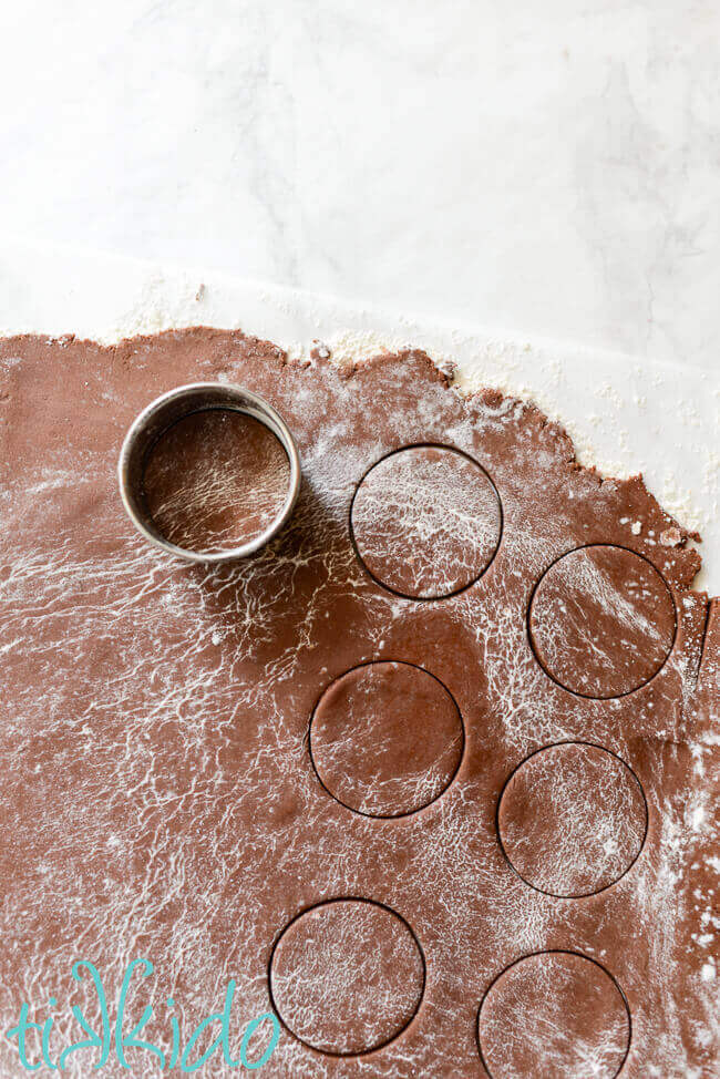 Homemade thin mint cookie dough being cut in circles on a marble surface.