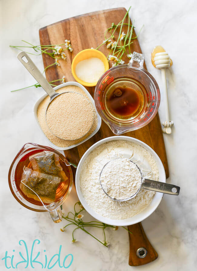 Ingredients for Chamomile Honey Cake on a wooden cutting board, on a white marble background