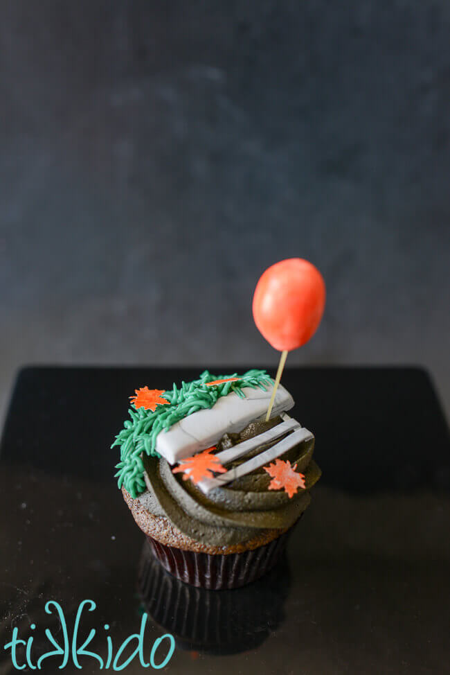 Chocolate cupcake with black chocolate icing topped with icing grass and a gum paste sewer grate with a gum paste balloon floating above the grate.  Inspired by the move IT.