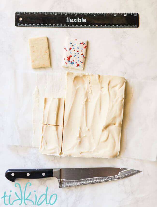 Square of frozen vanilla ice cream being cut into rectangular shapes for the centers of ice cream sandwiches.