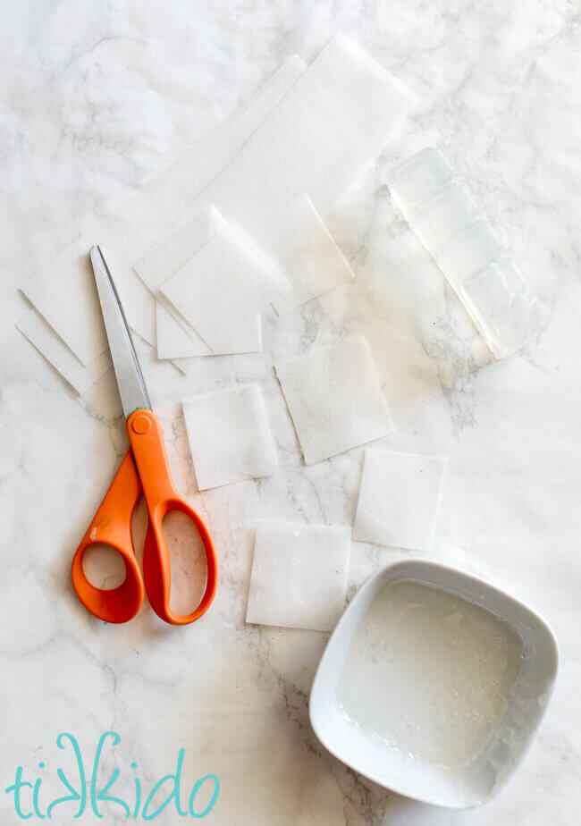 Wafer paper cut into squares next to a bowl with melted clear melt and pour soap base.