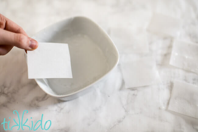 Square of wafer paper being dipped in melted melt and pour soap base to make Single Use Soaps