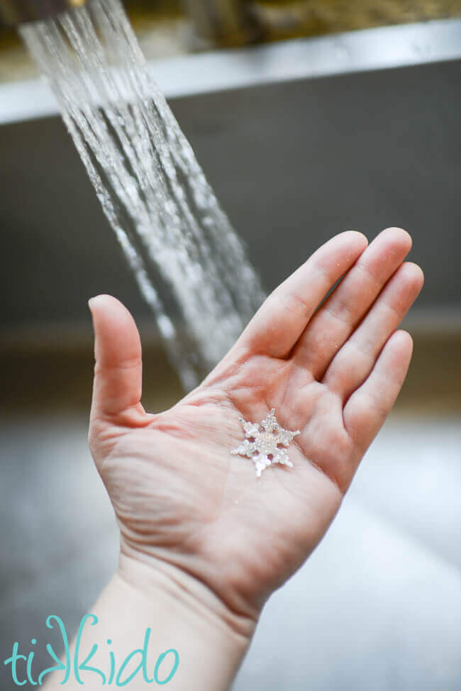 Single use snowflake soap on a hand in front of a stream of water in a sink.
