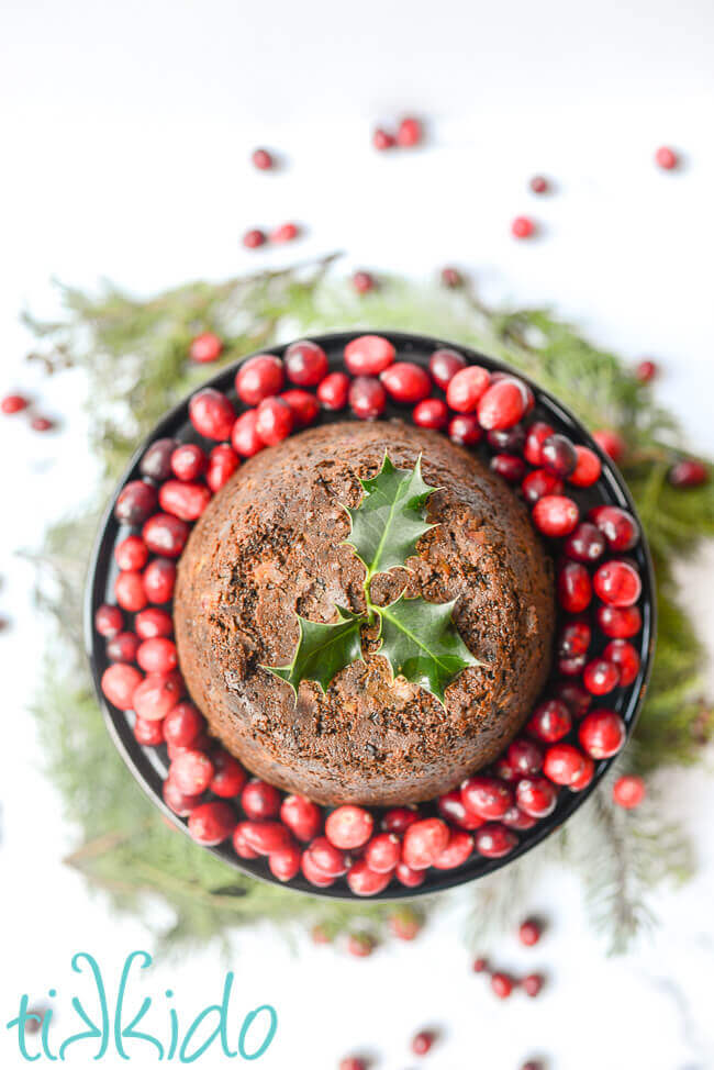 Cranberry Christmas pudding made in an instant pot, surrounded by fresh cranberries and topped with a sprig of holly.