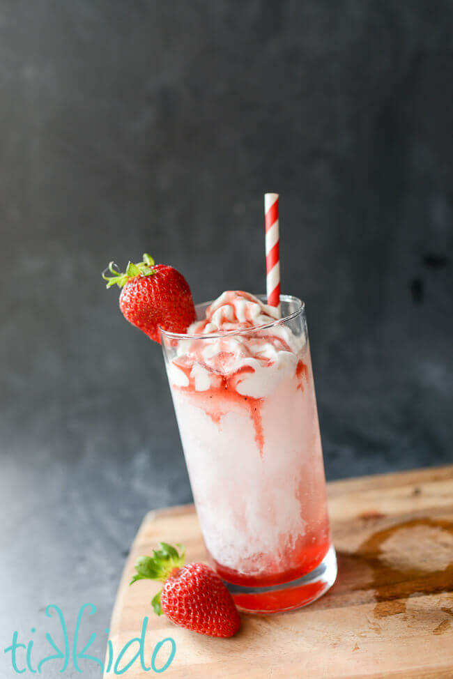 Strawberry Italian cream soda on a wooden cutting board on a black chalkboard background.