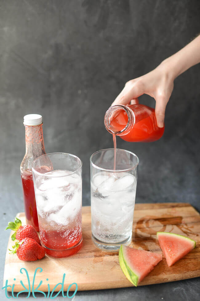 Simple syrup being poured in sparkling water to make homemade Italian Cream Sodas.