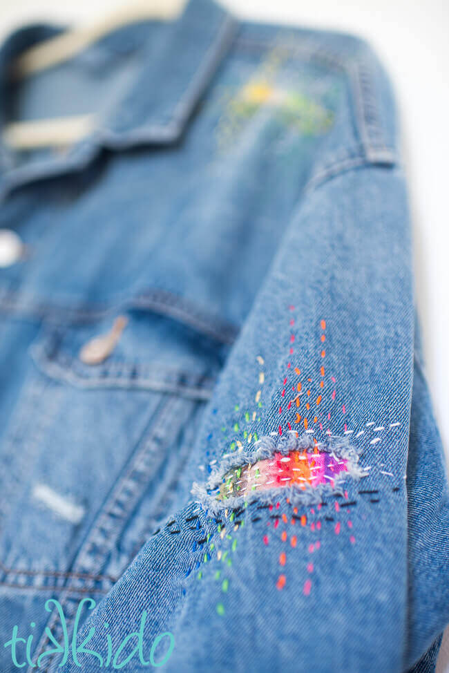 Hole in the arm of a jean jacket patched with colorful Sashiko mending.