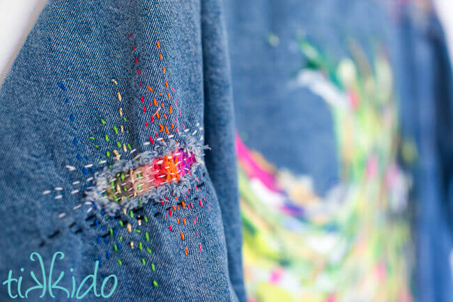 Hole in the arm of a jean jacket patched with colorful Sashiko mending.