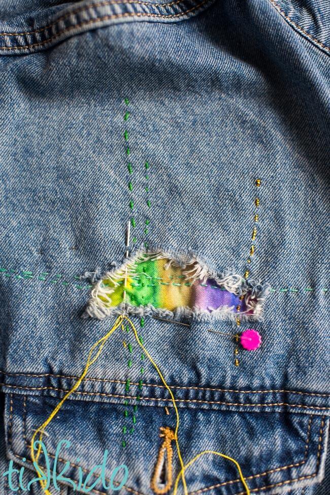 Horizontal and vertical lines of stitches being created on a jean jacket being mended with visual mending.