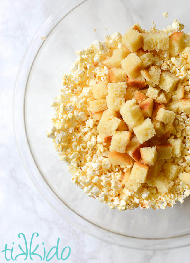 Cubed pound cake and crushed popcorn in a glass bowl on a white marble background.