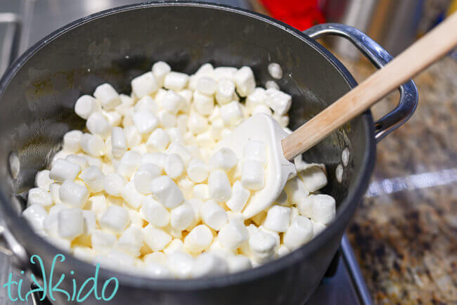 Marshmallows and butter being melted in a saucepan, with a spatula stirring the marshmallows.