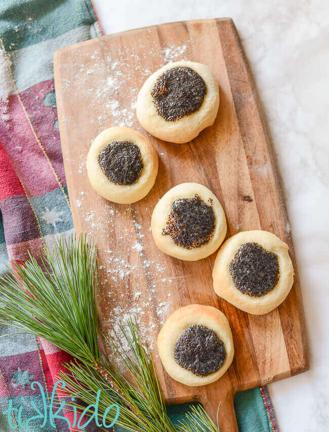 Poppy Seed Kolache on a wooden cutting board, next to a Christmas tea towel on a white marble surface.