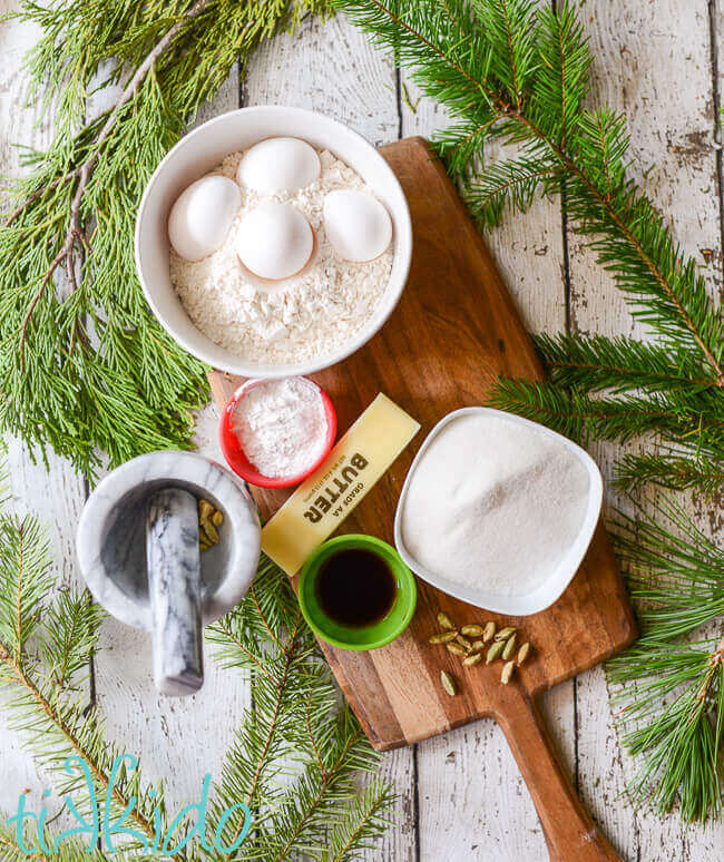 Ingredients for krumkake on a wooden cutting board surrounded by evergreen branches.