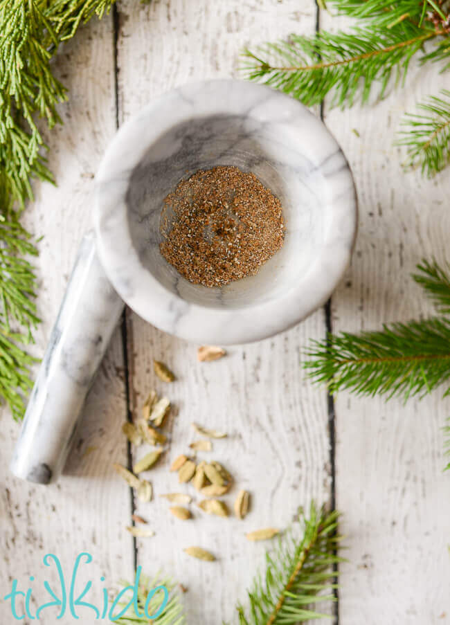 Freshly ground cardamom in a marble mortar and pestle on a white weathered wood background.