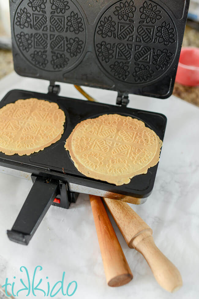 Golden brown, cooked Krumkake on the krumkake iron, ready to be rolled on the wooden forms.