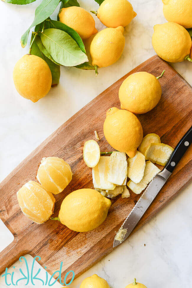 Lemons with the skin and pith cut from the fruit on a wooden cutting board.