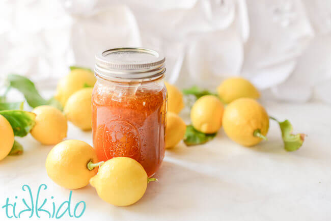 Homemade lemon jam in a mason jar surrounded by whole lemons