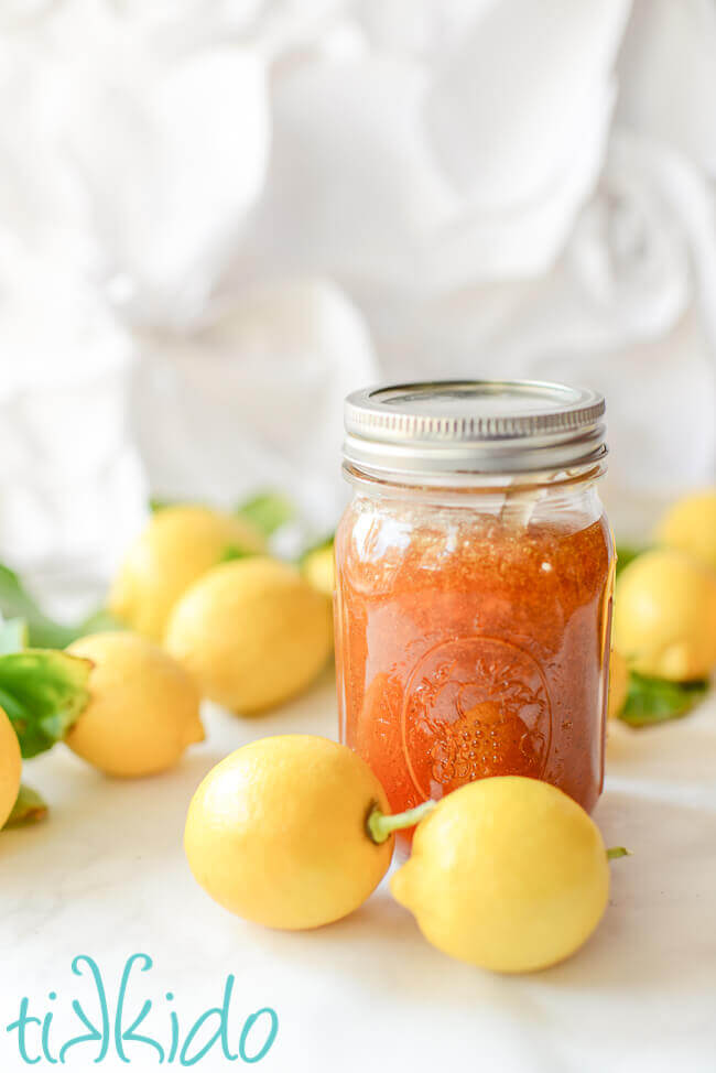 Homemade lemon jam in a mason jar, surrounded by whole lemons.