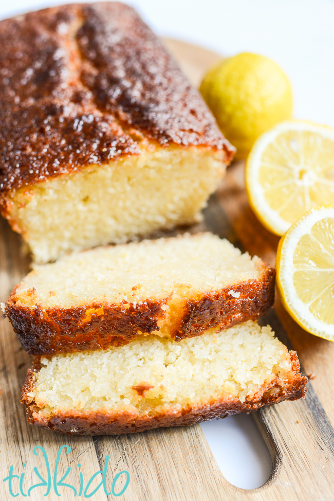 Lemon Loaf sliced on a wooden cutting board, next to a lemon sliced in half.