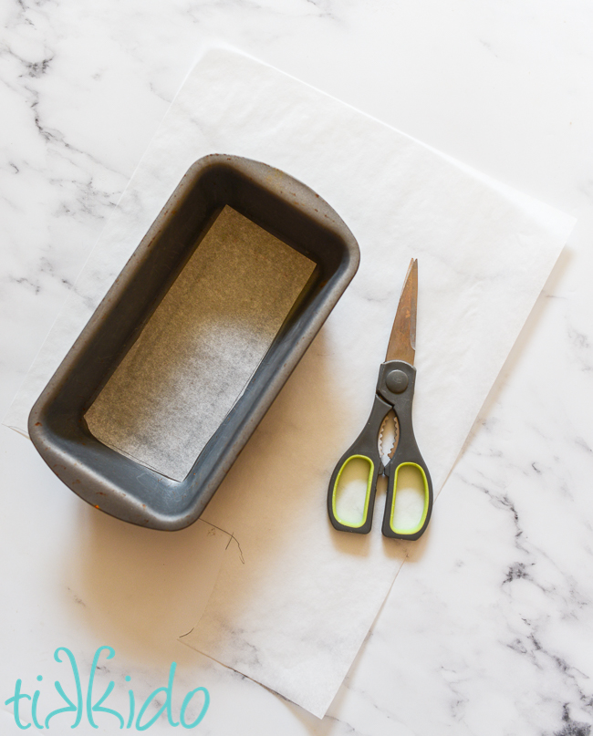 Bread loaf pan lined with parchment paper on a white marble surface.