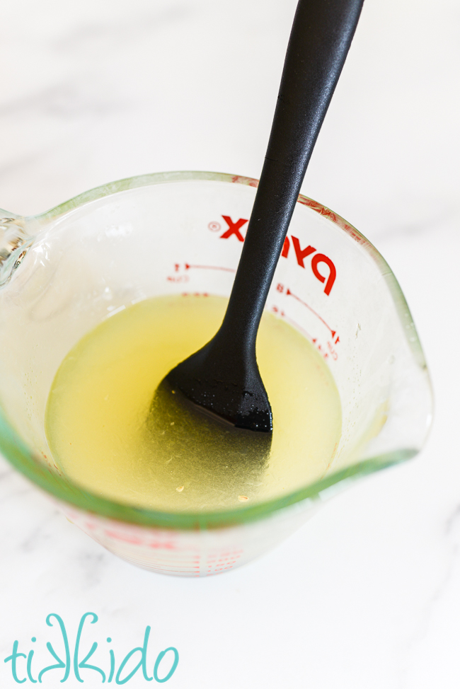 lemon glaze for lemon loaf cake being mixed in a pyrex measuring cup with a black spatula.