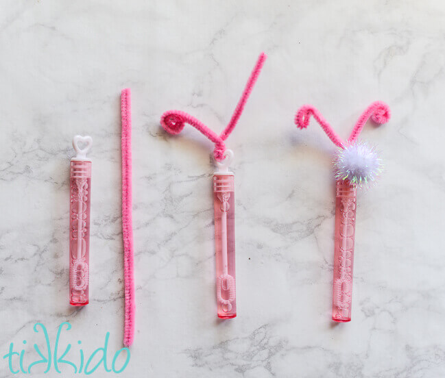 Small pink bubble wand and pink pipe cleaner being twisted around top of bubble wand to make butterfly antennae