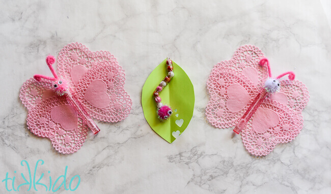 Two butterfly bubbles valentines and one chocolate sixlet caterpillar valentine on a white marble background