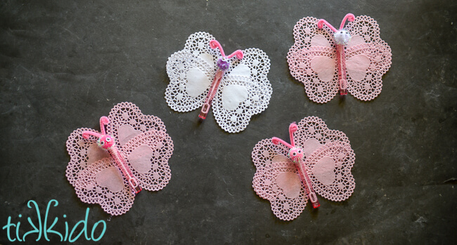 Four butterfly bubbles valentines made with heart shaped doilies and bubble wands on a black background.