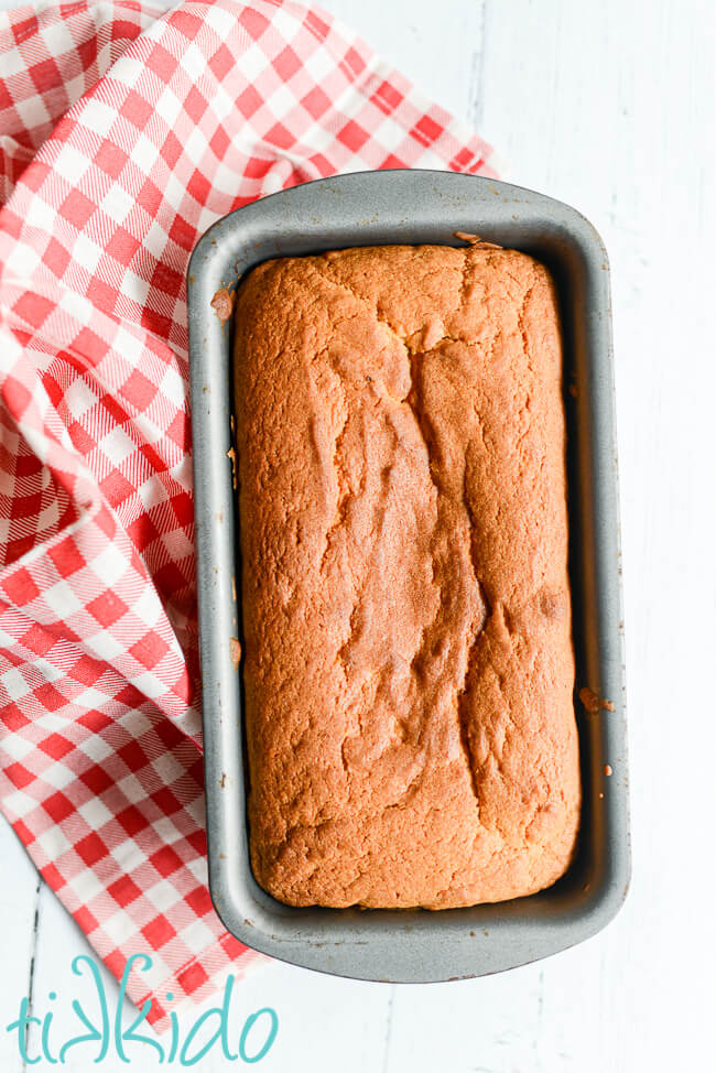 Madeira loaf Cake baked in a bread loaf tin, on a white wooden surface, next to a red and white gingham tea towel.