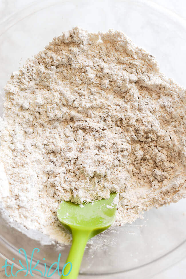 Mixture of ingredients for Chocolate Malt Tootsie Roll candies in a glass bowl with a green spatula.