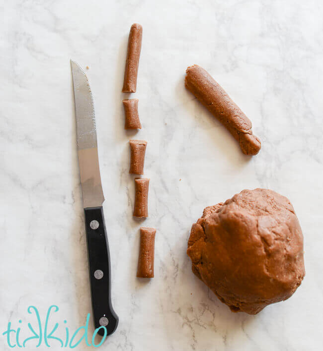 Ball of homemade tootsie roll next to tootsie roll dough rolled into a log and cut into pieces, sharp knife next to cut pieces