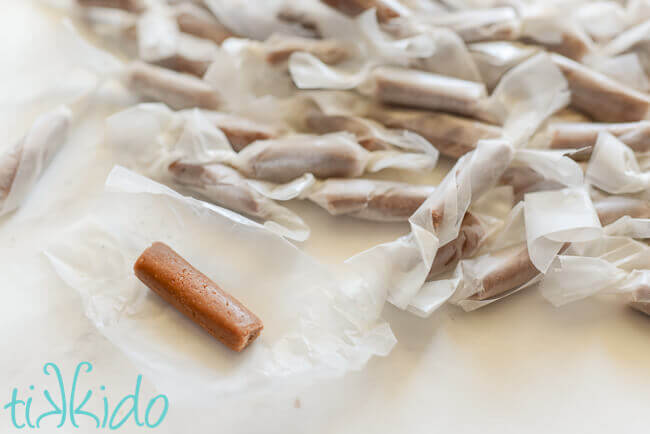 Pile of homemade malted chocolate tootsie roll candies wrapped in waxed paper, with one unwrapped candy next to the pile.