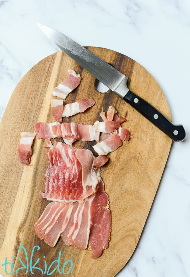 Bacon being sliced into small pieces on a wooden cutting board for making Maple Bacon Popcorn.