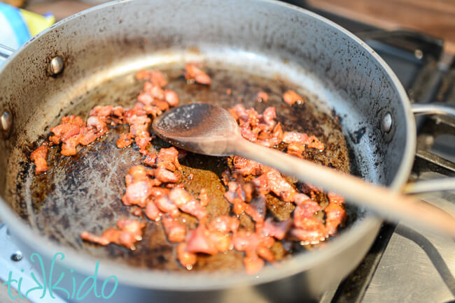 Bacon bits being cooked in a large frying pan.