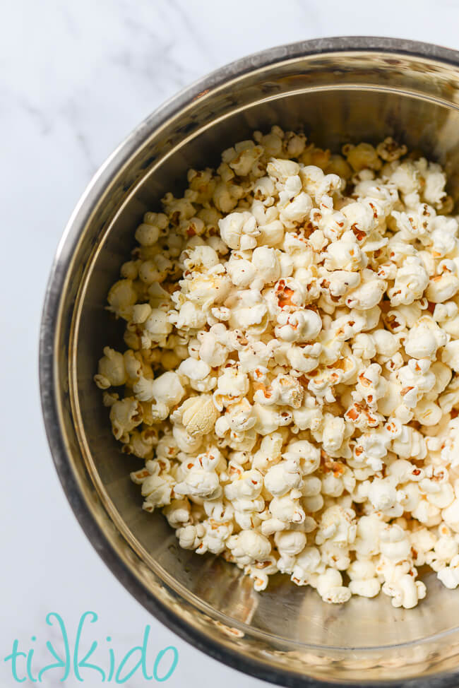 Popcorn popped in bacon grease in a large silver mixing bowl on a white marble table.