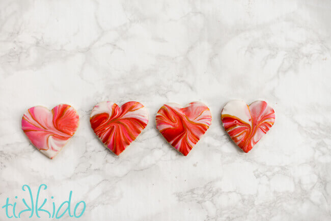 Four heart shaped sugar cookies dipped in marbled royal icing in reds and pinks for Valentine's day.