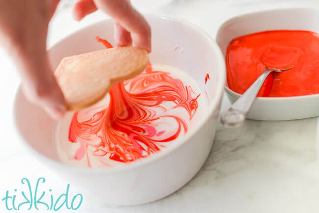 Sugar cookie being dipped in marbled royal icing to create marbleized cookies.