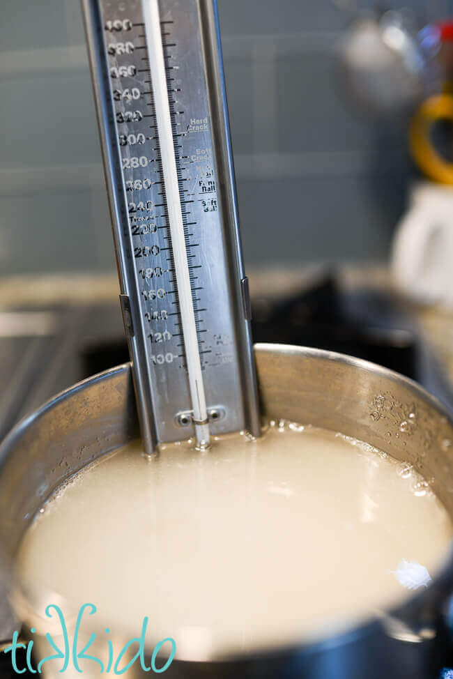 Homemade marshmallow sauce being cooked in a pot on the stovetop, with a candy thermometer in the liquid.