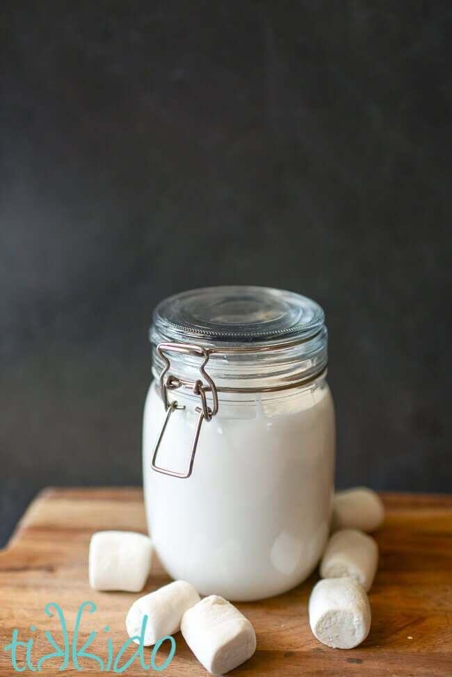 Homemade marshmallow sauce in a glass jar, surrounded by marshmallows