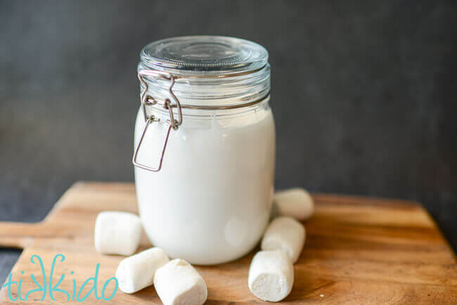 Homemade marshmallow sauce in a glass jar, surrounded by marshmallows