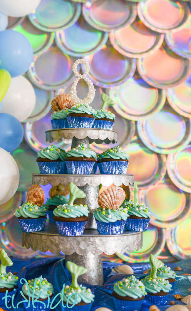 Cake stand covered with cupcakes topped with chocolate seashells and chocolate mermaid tails.