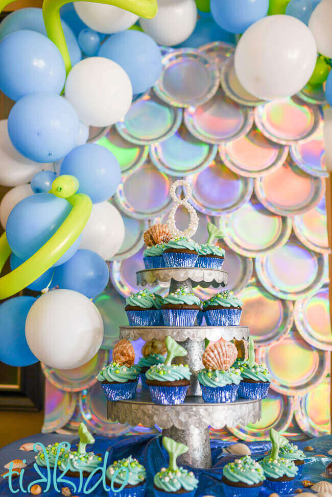 Three tiered cake stand covered with mermaid and seashell topped cupcakes.