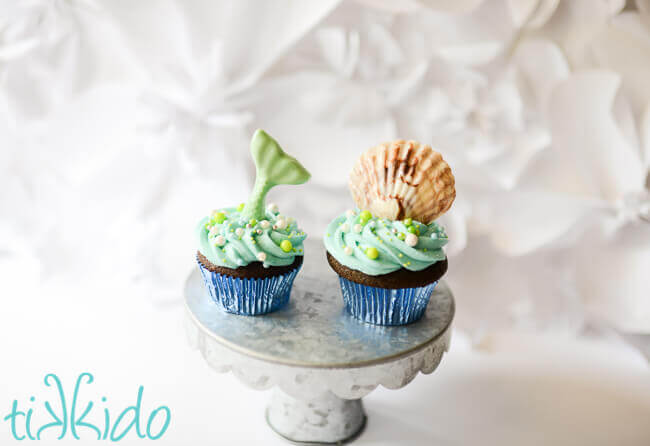 Chocolate seashell cupcake and chocolate mermaid tail cupcake on a silver cake stand.