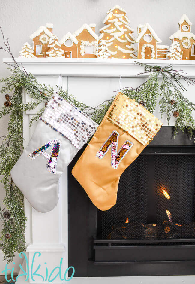 Christmas stockings with mermaid sequin reversible fabric monograms on silver and gold stockings on a white fireplace mantle.