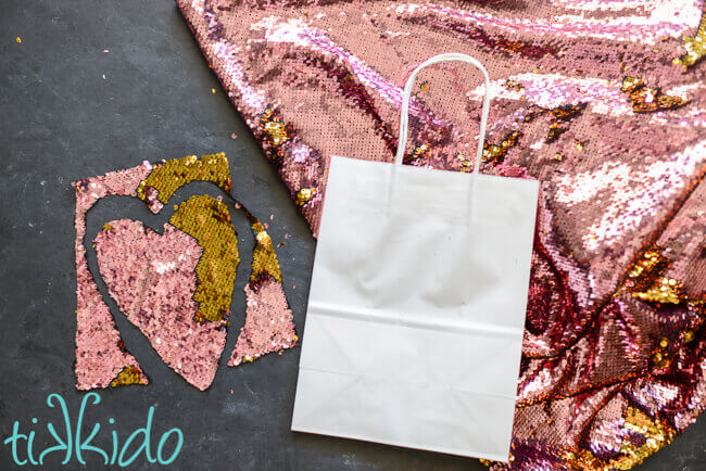 pink and gold mermaid sequin fabric cut into a heart shape and a plain white gift bag.
