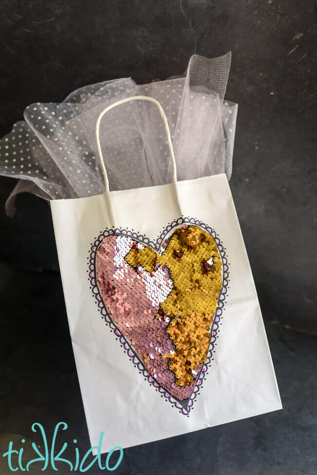 white gift bag with pink and gold mermaid fabric heart on a black chalkboard background.