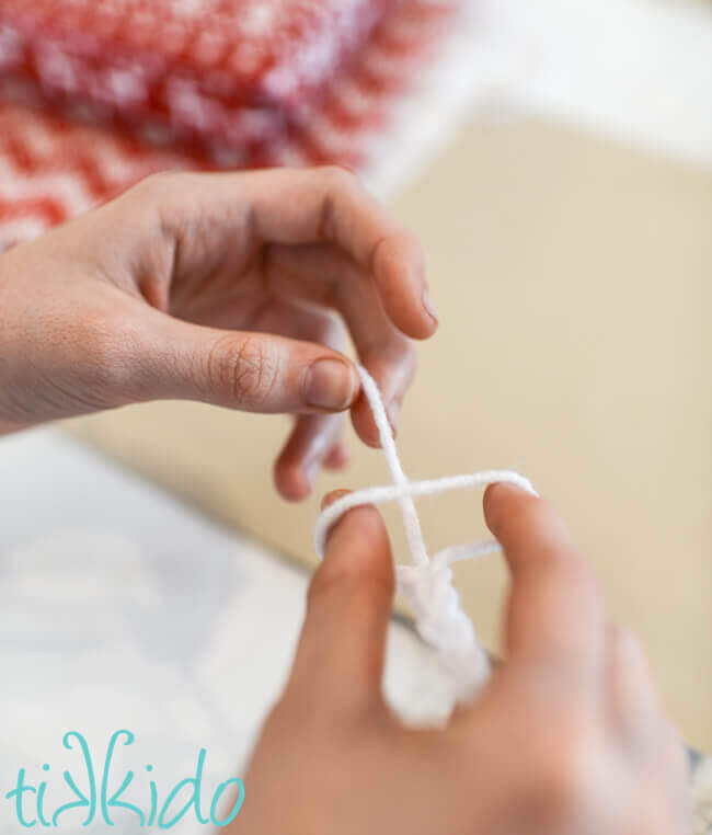 Fingers creating a simple chain with white yarn.