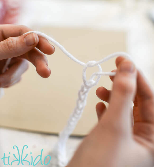 Fingers creating a simple chain with white yarn.