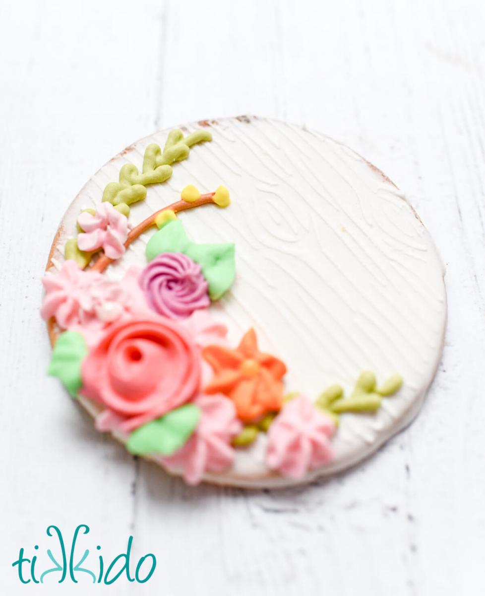 Closeup of a sugar cookie decorated with a wood grain stencil pattern and a collection of bright spring flowers made from royal icing.