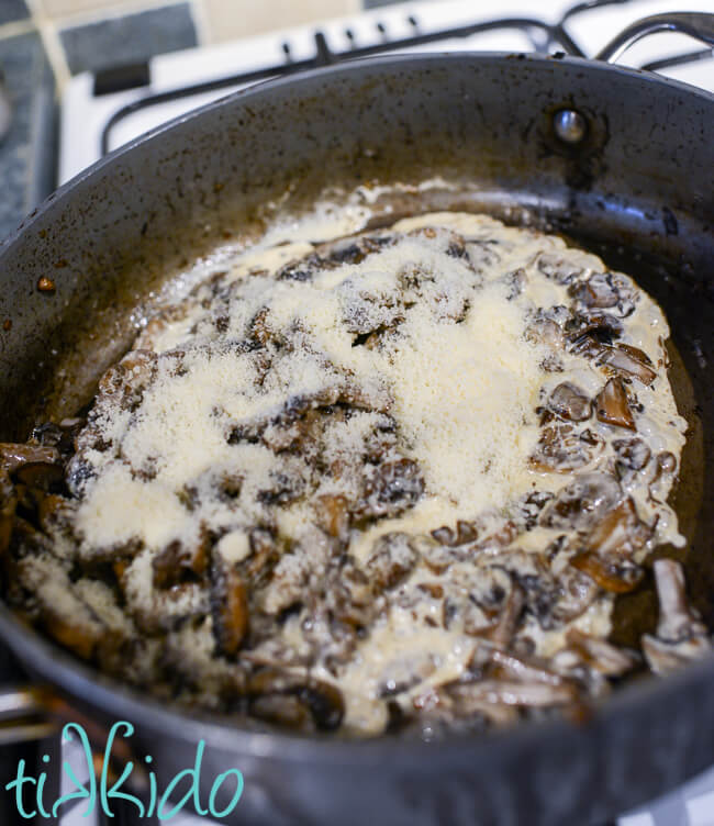 Cooked mushrooms being mixed with cream and parmesan in a saucepan to make mushrooms on toast.